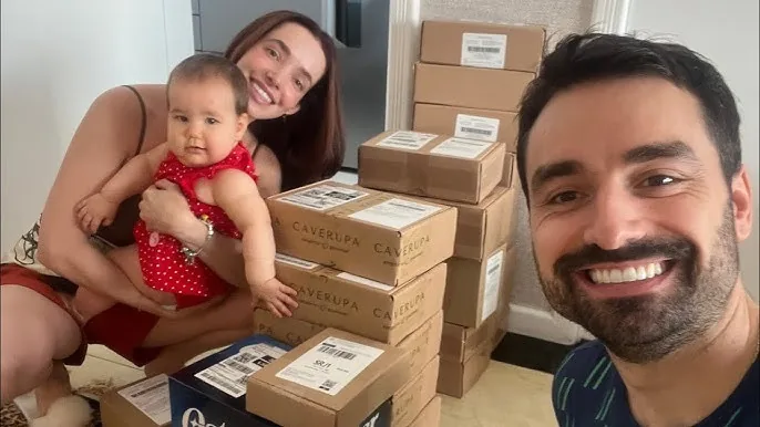 O Vitor, a esposa e a filha bebê entre caixas de pedidos na sala de casa
